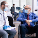 Doctor With Face Mask Stethoscope Consulting Disabled Senior Man Hospital Waiting Area 150x150